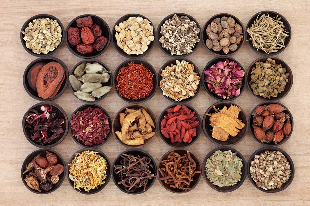 An assortment of traditional Chinese herbs is displayed in small wooden bowls